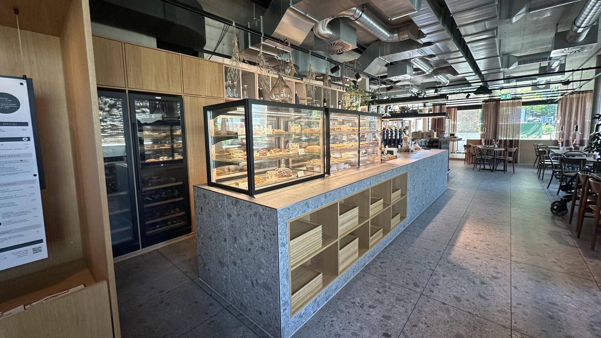 Theke mit Gebäckauslage, Weinkühlschrank und Holzschränken in einem hellen, modernen Cafébereich.