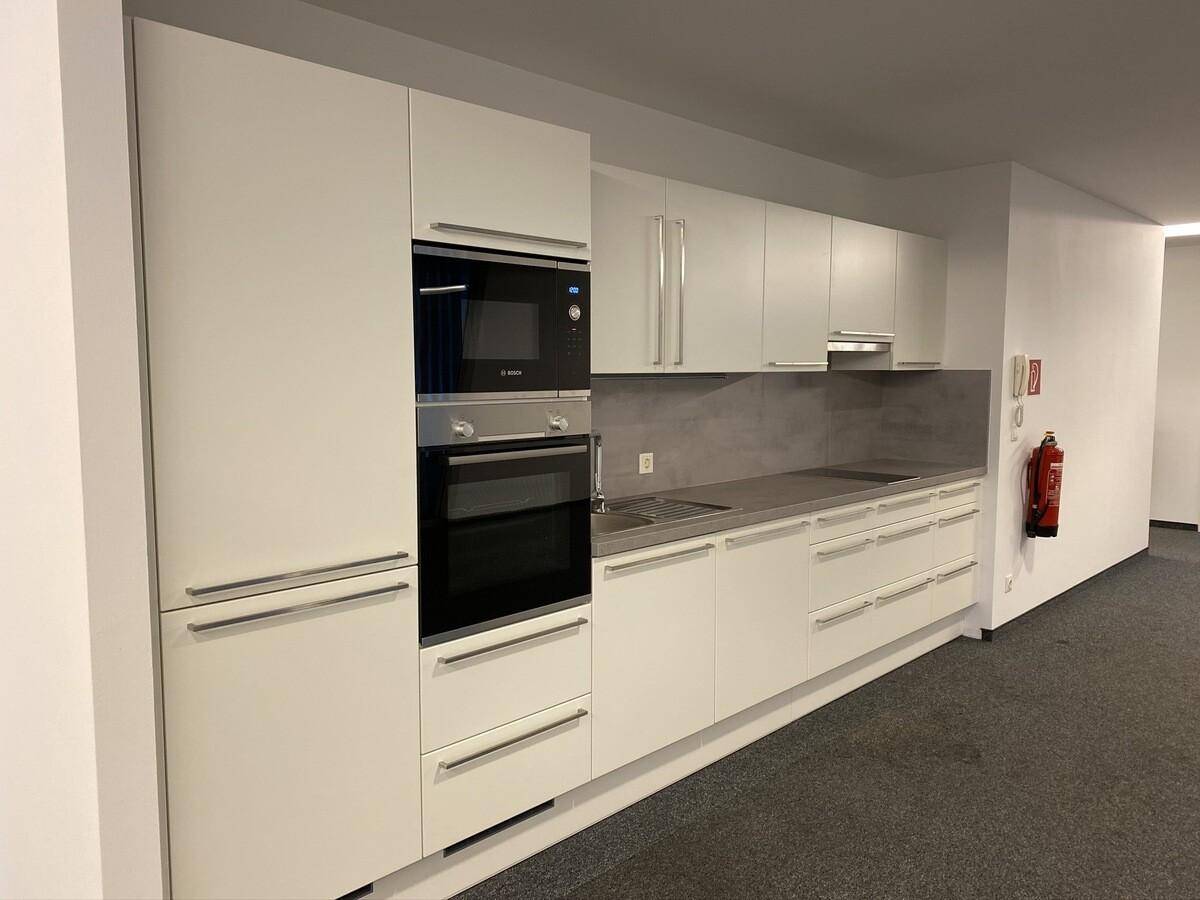 Moderne Küchenzeile mit weißen Schränken, integriertem Backofen und Mikrowelle sowie dunkler Arbeitsplatte und Bosch-Geräten.
