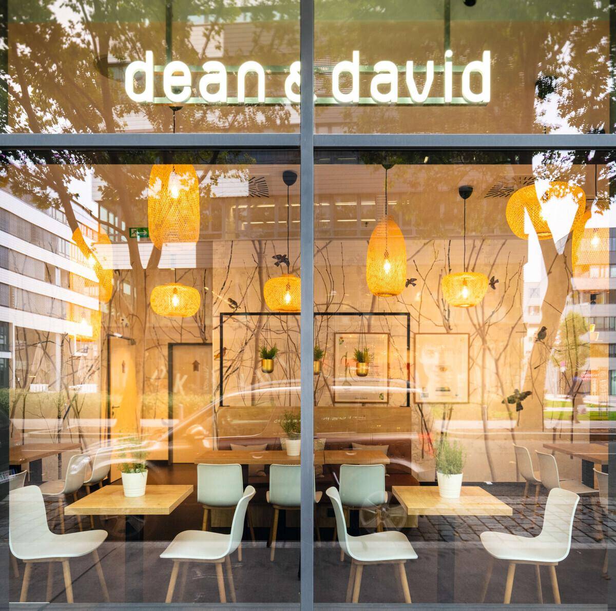 Einladendes Restaurantinterieur mit Holztischen, modernen Stühlen und dekorativen Hängelampen, sichtbar durch die Glasfront.