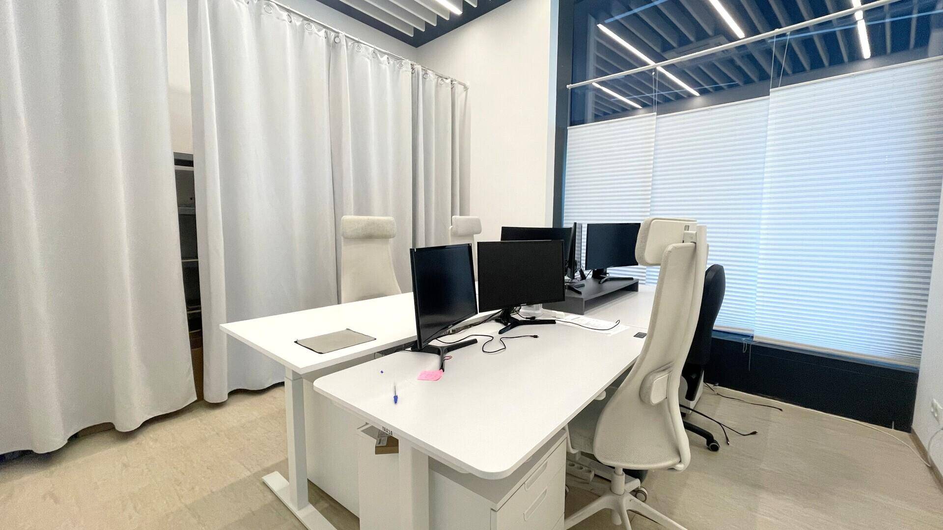 Ruhiger Bürobereich mit weißen Vorhängen, modernen Arbeitsplätzen und ergonomischen Bürostühlen für konzentriertes Arbeiten.