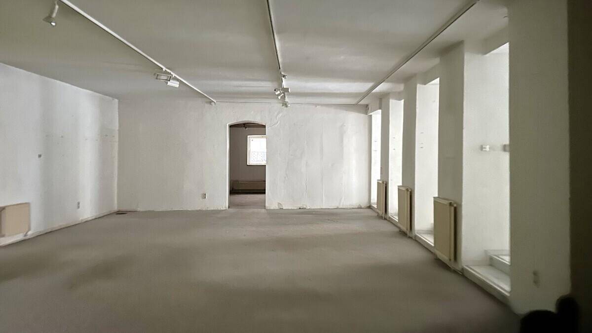 Leerer Raum mit weißen Wänden, Teppichboden und einem Fenster, das natürliches Licht hereinlässt.