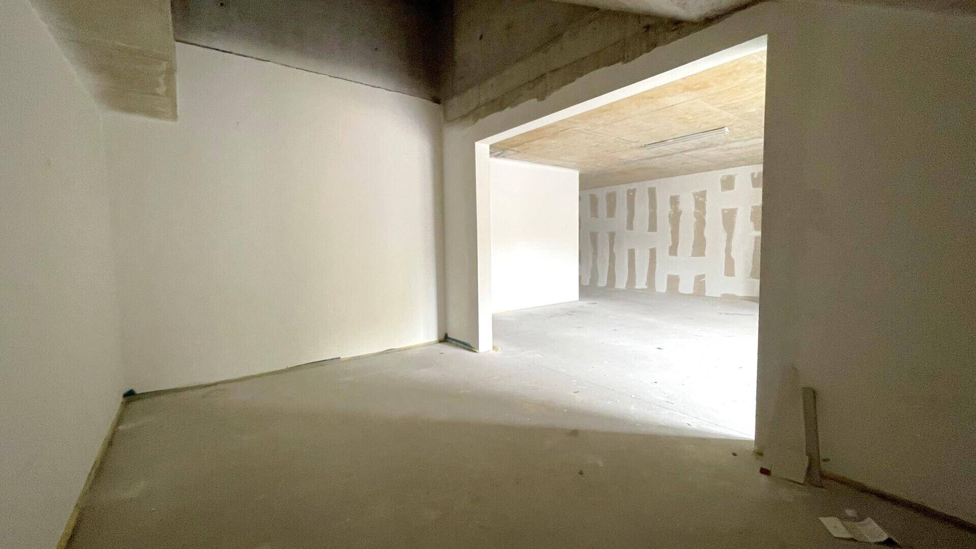 Weiterer Blick in den unfertigen Innenraum mit offenem Durchgang zu einem angrenzenden Bereich und Betonoberflächen.