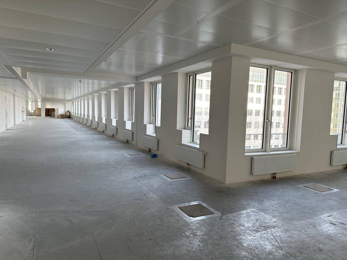 Langer, heller Bürogang mit zahlreichen Fenstern und Bodenzugangspaneelen für flexible Arbeitsplatzgestaltung.
