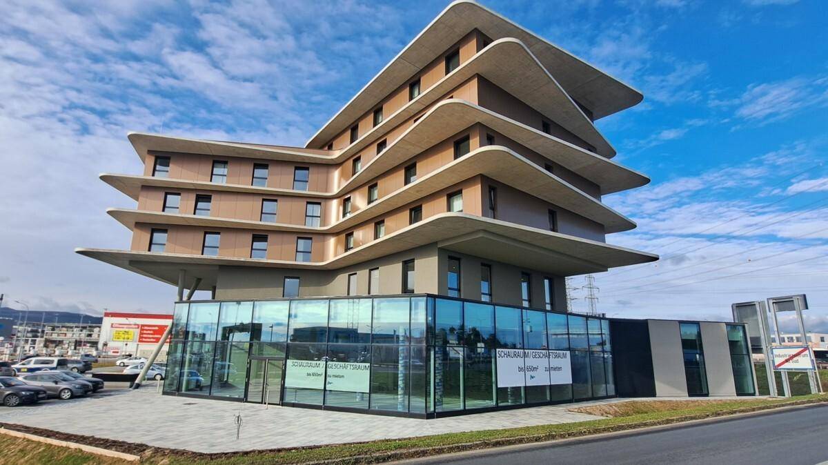 Gesamtansicht des markanten, modernen Gebäudes mit seinen geschwungenen Etagen und der Glasfassade unter blauem Himmel.