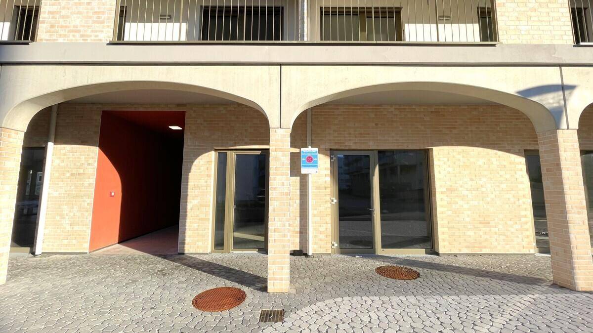 Erdgeschossfassade eines modernen Gebäudes mit Arkaden, großen Fenstern und einem Eingangsbereich.