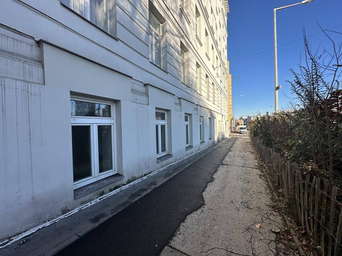 Seitenansicht des Gebäudes mit Fenstern und einem schmalen Gehweg entlang der Fassade.