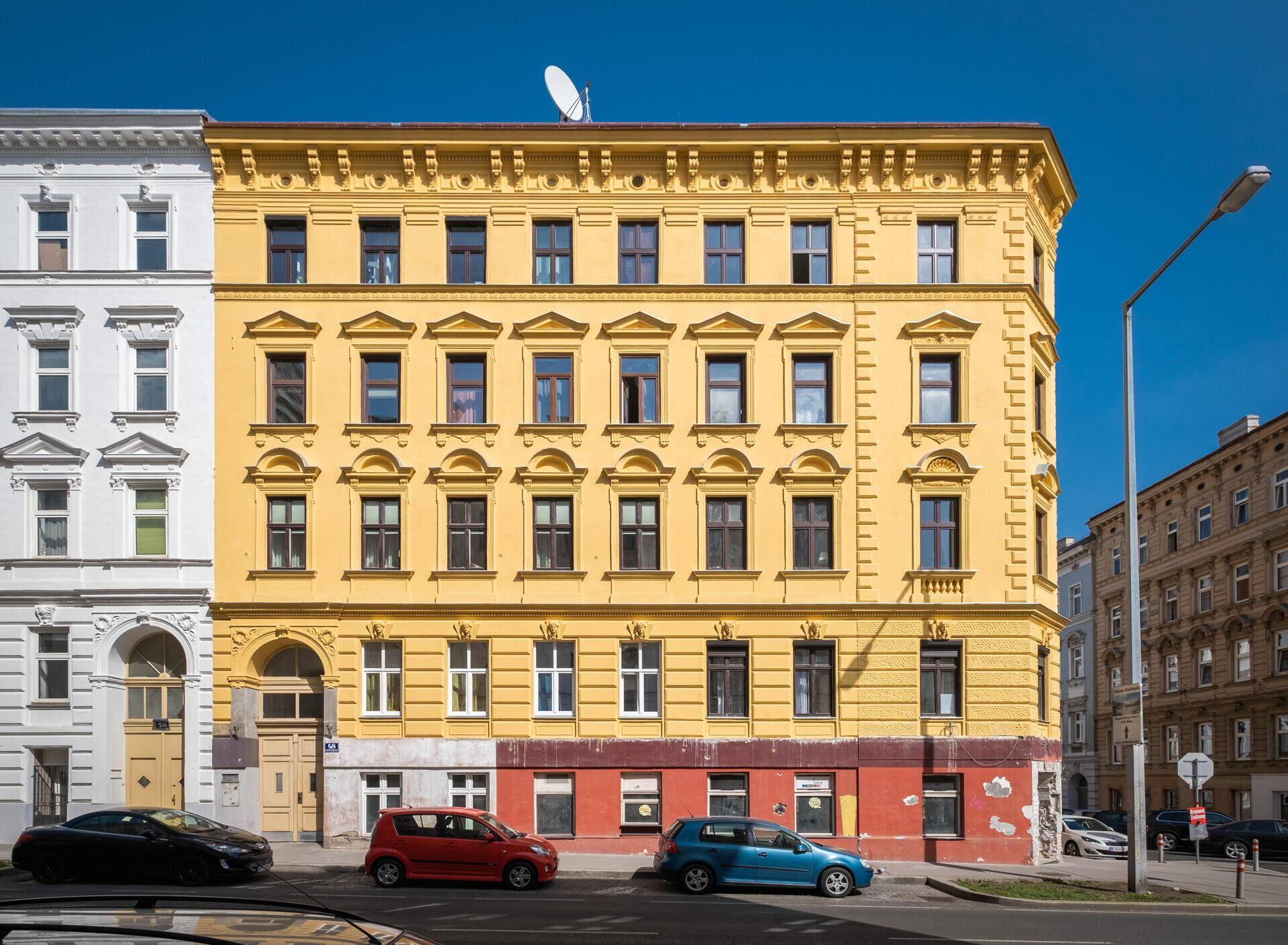 Detailansicht der gelben Fassade eines historischen Gebäudes mit vielen Fenstern und Autos davor.