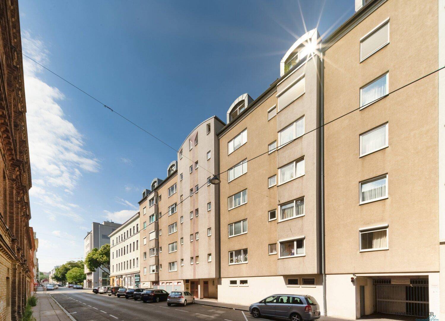 Mehrfamilienhaus mit moderner Fassade und vielen Fenstern an einer städtischen Straße.