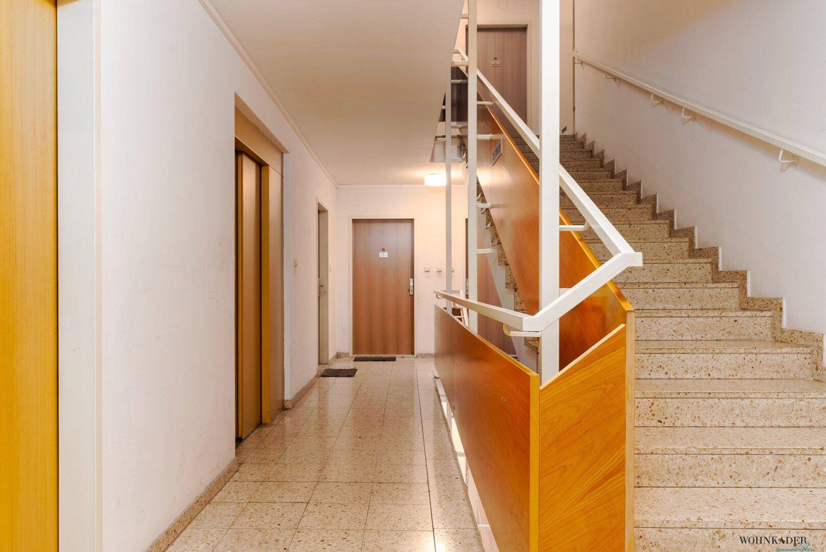 Treppenhaus und Flur mit Aufzug, Terrazzoboden und Zugang zu den Wohnungen.