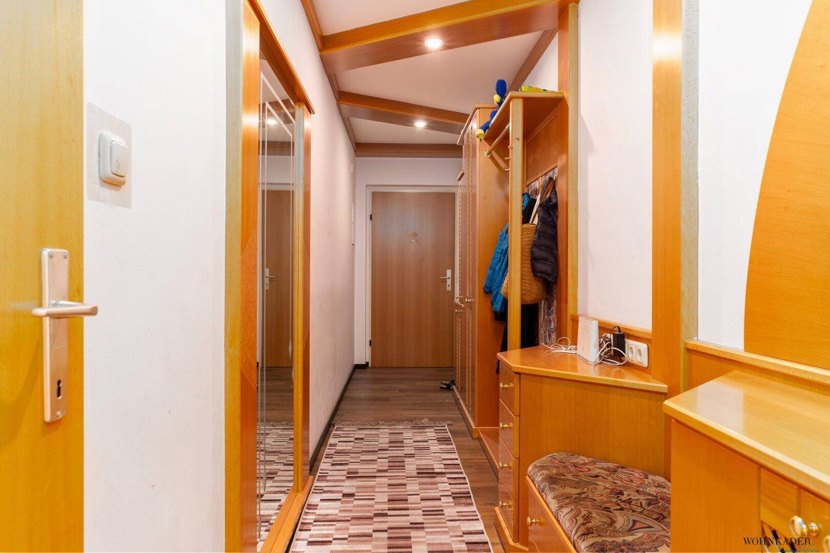 Heller Eingangsbereich mit Holzelementen, Garderobe und einem langen Spiegel.