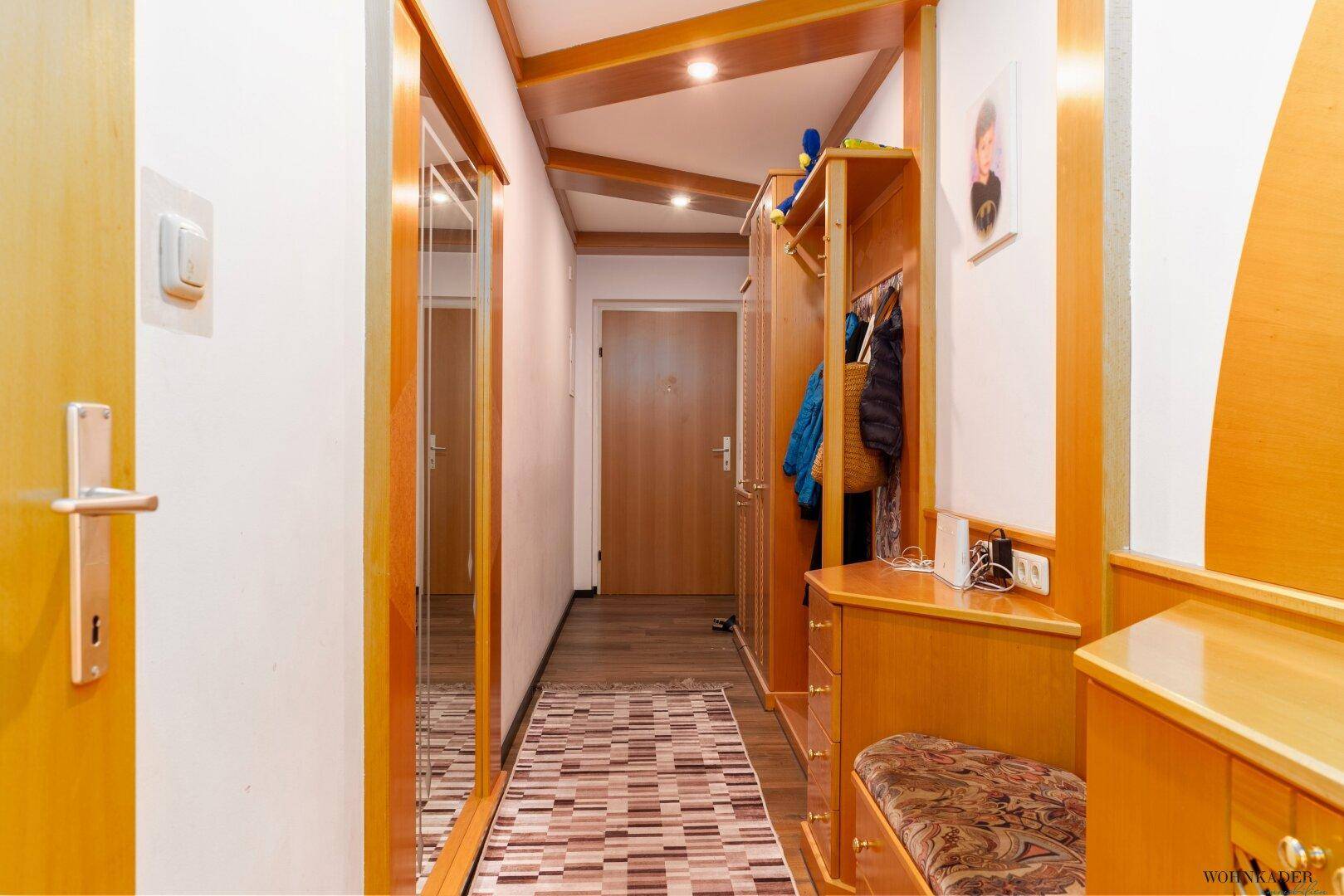Heller Eingangsbereich mit Holzelementen, Garderobe und einem langen Spiegel.