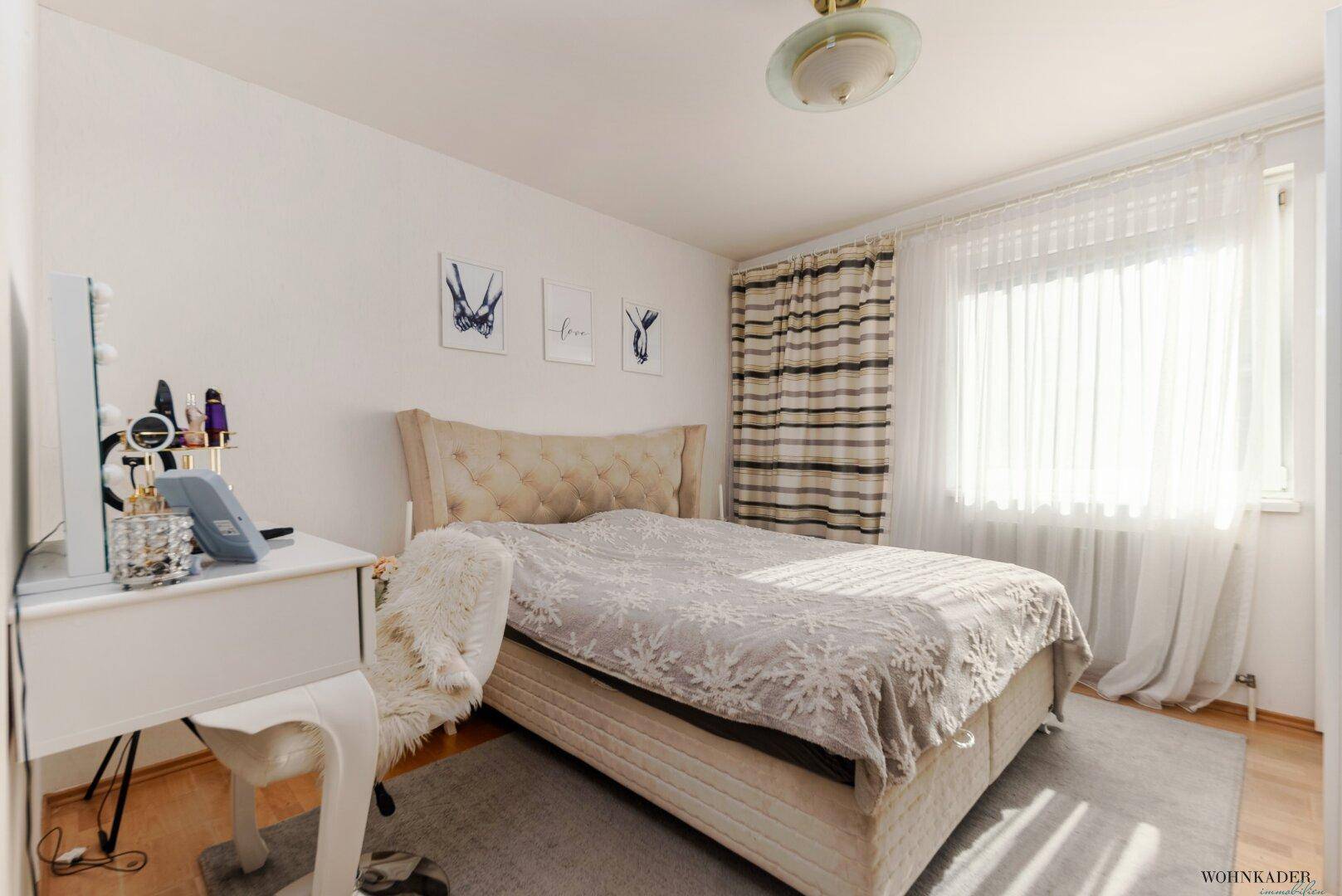 Gemütliches Schlafzimmer mit Doppelbett, Schminktisch und großem Fenster für viel Tageslicht.