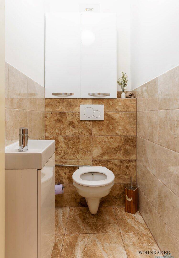 Kleines Gäste-WC mit beigen Fliesen, wandhängendem WC und einem kompakten Waschbecken.