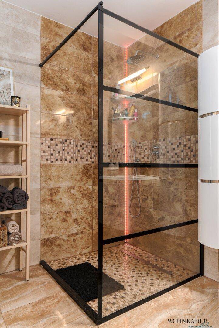 Moderne begehbare Dusche mit Glaswänden und beigen Fliesen, ausgestattet mit Duschprodukten.