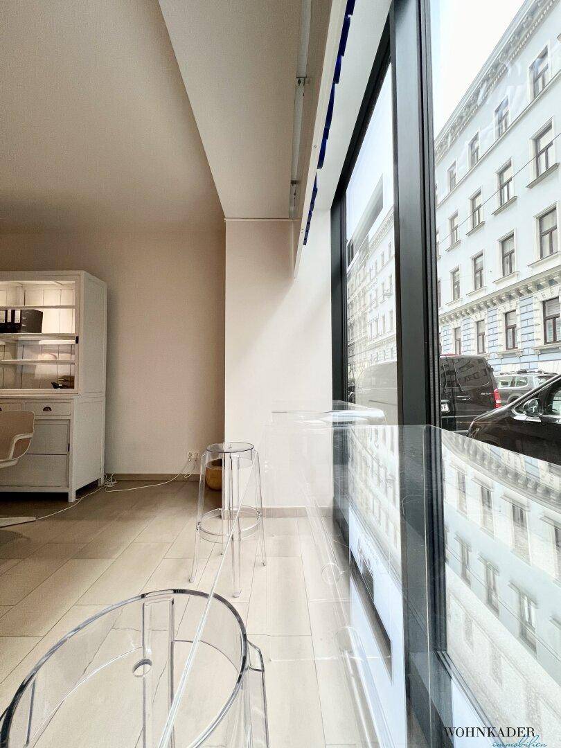 Blick entlang der Fensterfront des Büros mit transparenten Hockern und der gegenüberliegenden Bebauung.