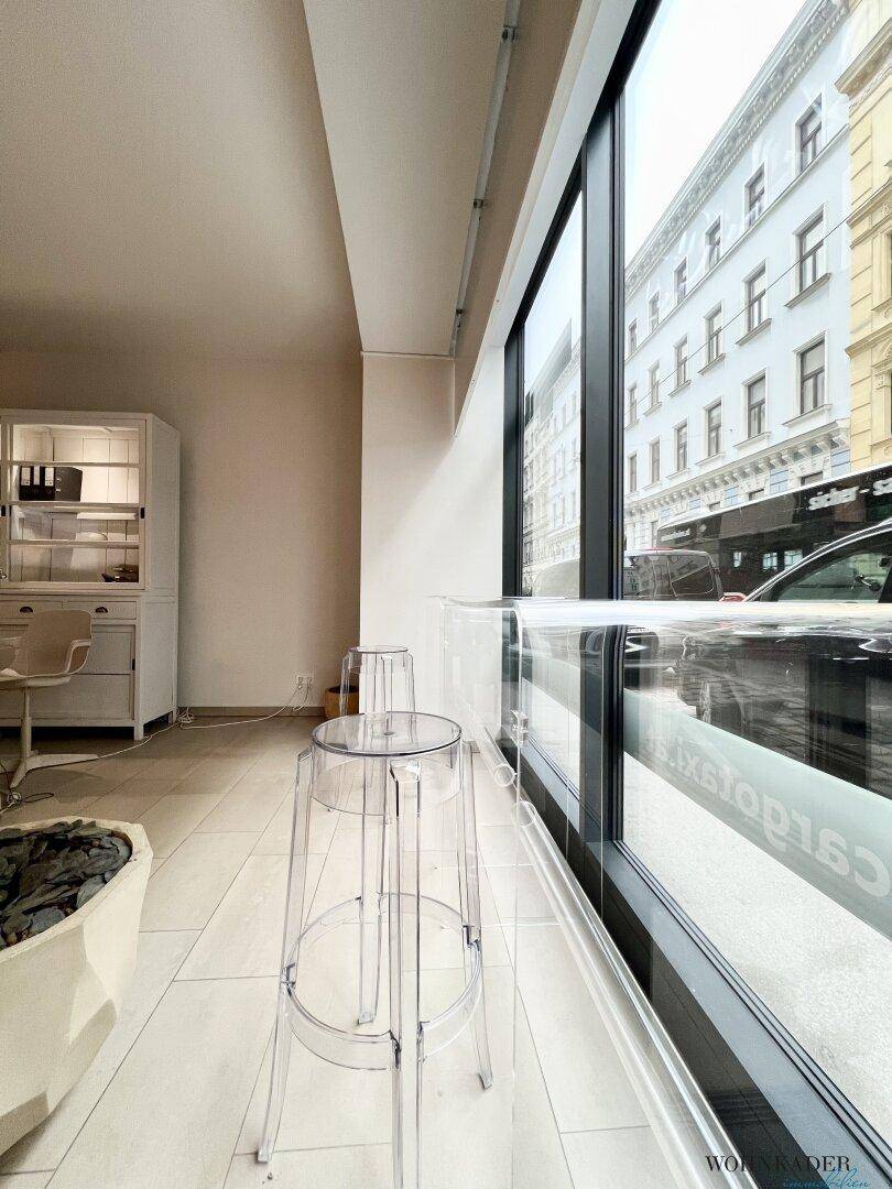 Blick entlang der Fensterfront des Büros mit transparenten Hockern und der gegenüberliegenden Bebauung.