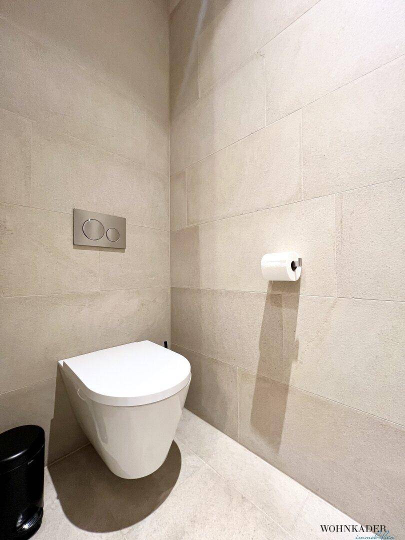 Modernes Gäste-WC mit wandhängender Toilette und hellen Fliesen an Wänden und Boden.