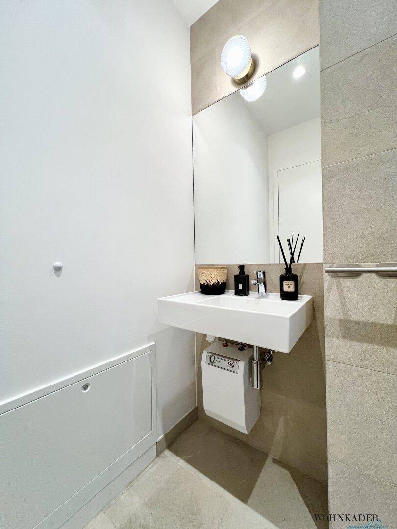 Modernes Gäste-WC mit Waschbecken, Spiegel und indirekter Beleuchtung, in hellen Farbtönen gehalten.