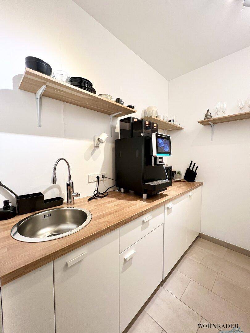 Kleine, funktionale Küchenzeile mit Spüle, Holz-Arbeitsplatte und integrierter Kaffeemaschine.