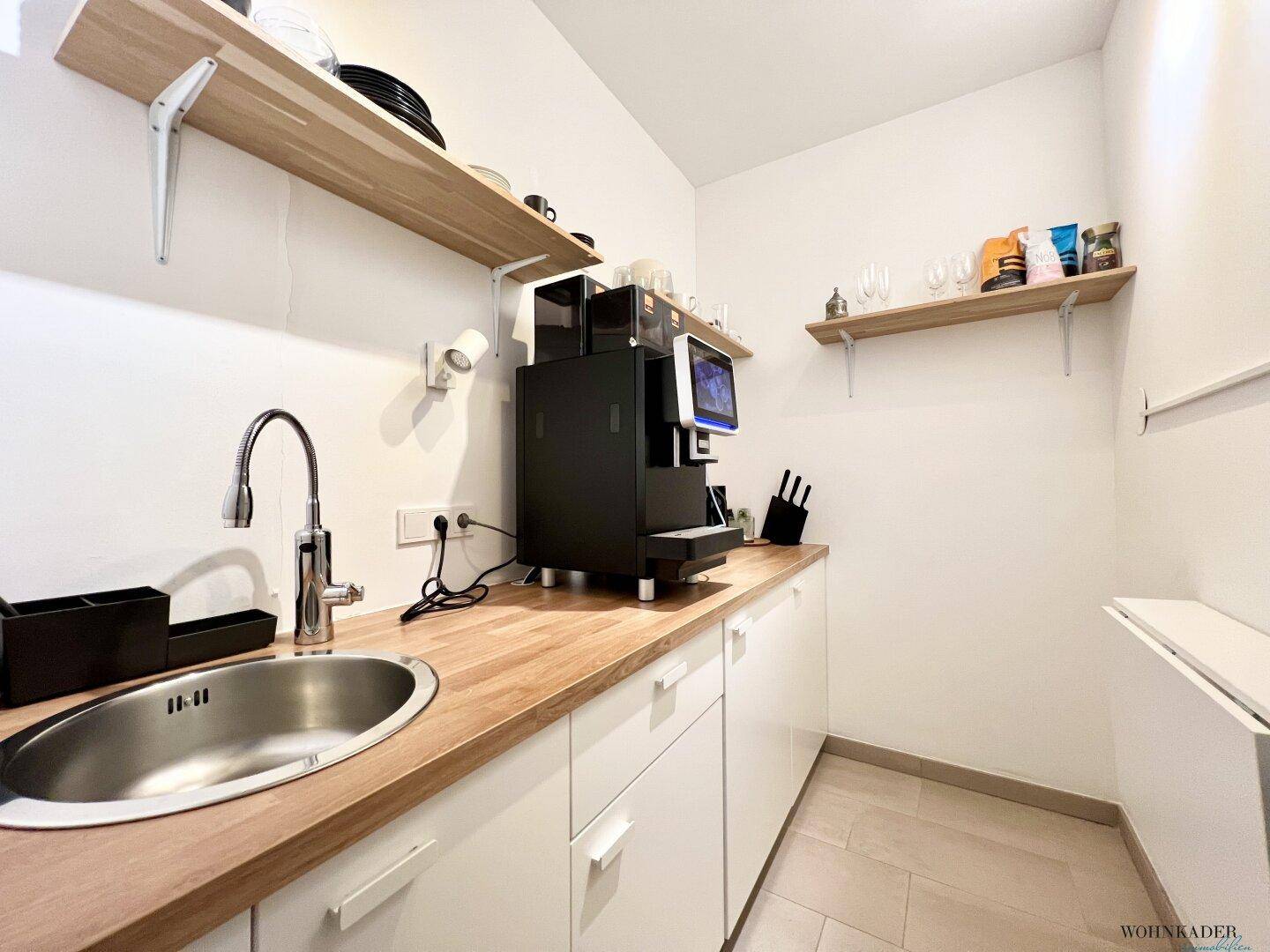 Kleine, funktionale Küchenzeile mit Spüle, Holz-Arbeitsplatte und integrierter Kaffeemaschine.