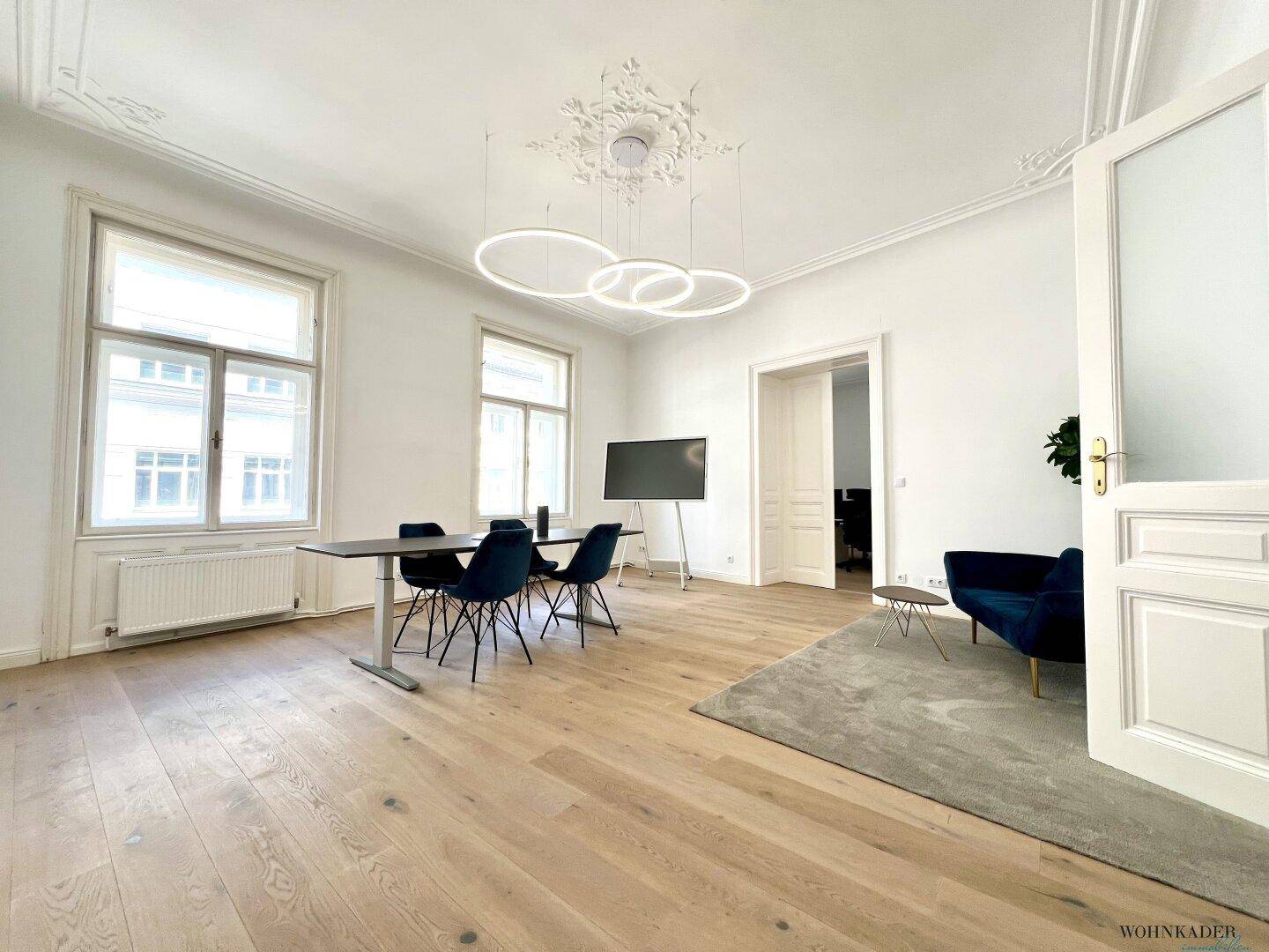 Vielseitiger Büroraum mit Besprechungsbereich und gemütlicher Lounge-Ecke, ausgestattet mit Holzboden und hohen Decken.