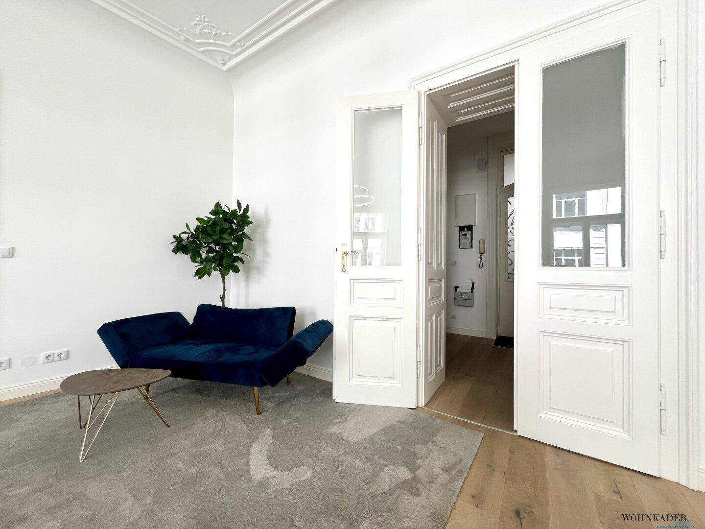 Gemütliche Lounge-Ecke im Bürobereich mit einem blauen Samtsofa, Beistelltisch und einer Zimmerpflanze.