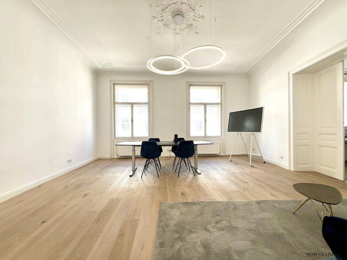 Großzügiger Büroraum mit Besprechungsbereich und entspannter Sitzecke, gekennzeichnet durch helle Wände und Holzboden.