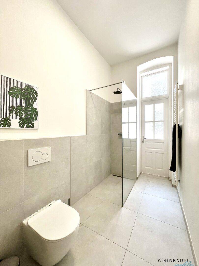 Heller Badezimmerbereich mit wandhängendem WC und einer geräumigen, begehbaren Dusche mit Glasabtrennung.