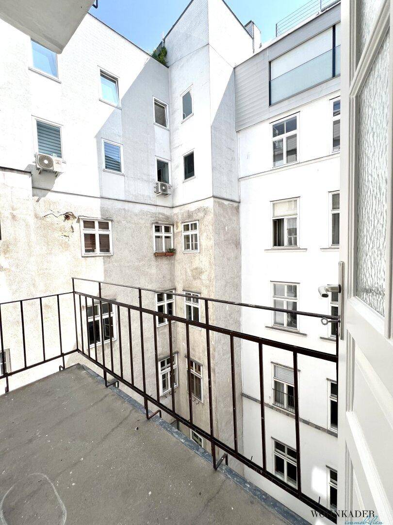 Kleiner Balkon mit Blick auf einen ruhigen Innenhof, umgeben von Gebäudefassaden.
