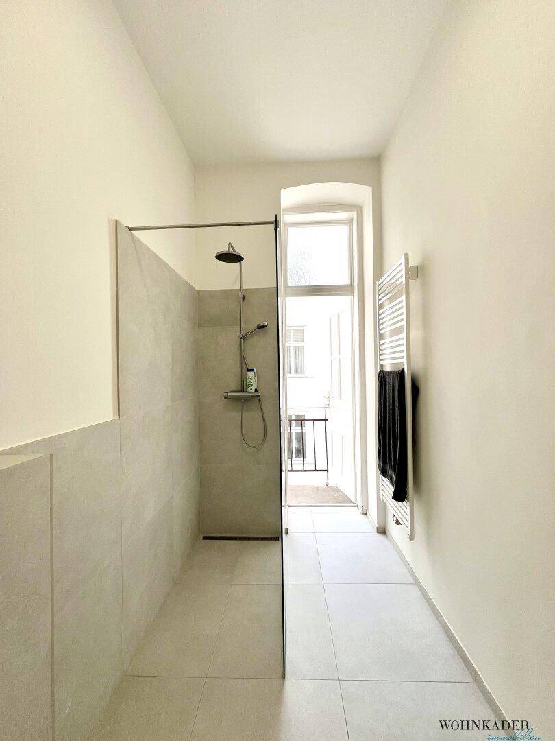 Begehbare Dusche im modernen Badezimmer mit Blick auf die Balkontür und den Handtuchheizkörper.
