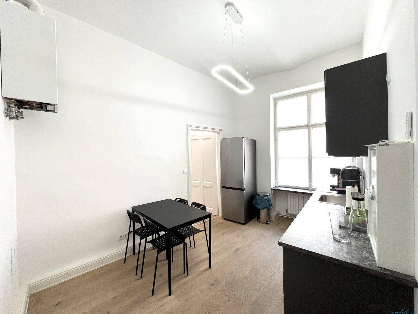 Funktionale Küche mit dunklen Schränken, Kühlschrank und kleinem Esstisch, ideal für eine schnelle Mahlzeit.