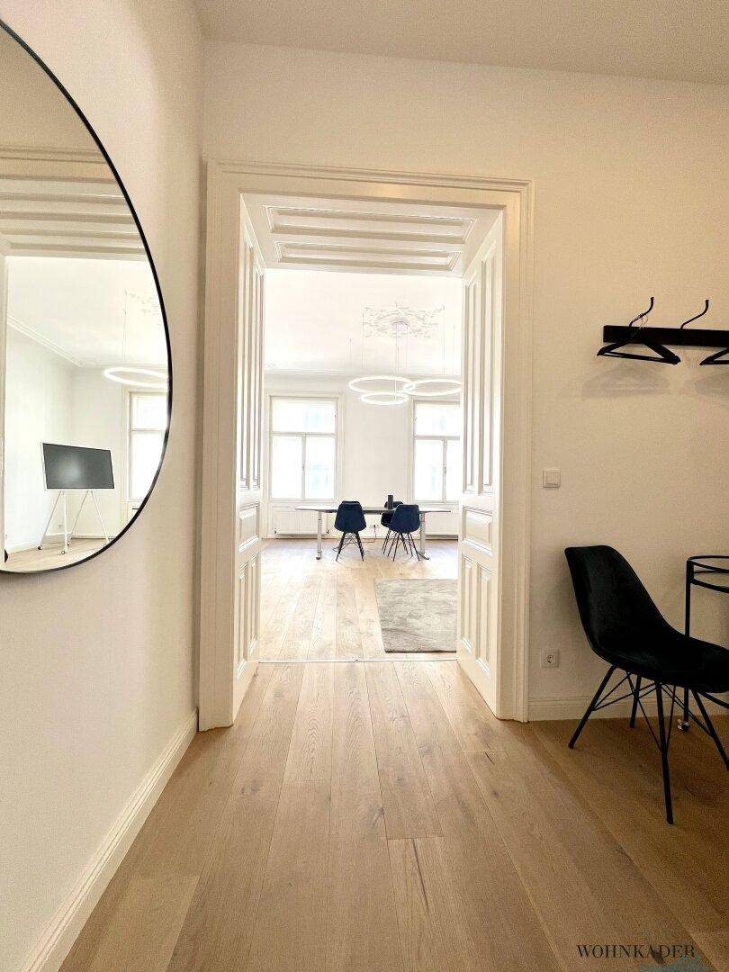 Eleganter Flur mit großem Rundspiegel, der einen Blick in den angrenzenden Büroraum freigibt.