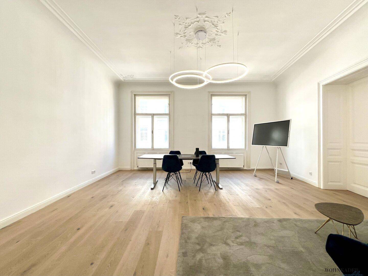 Großzügiger Büroraum mit Besprechungsbereich und entspannter Sitzecke, gekennzeichnet durch helle Wände und Holzboden.