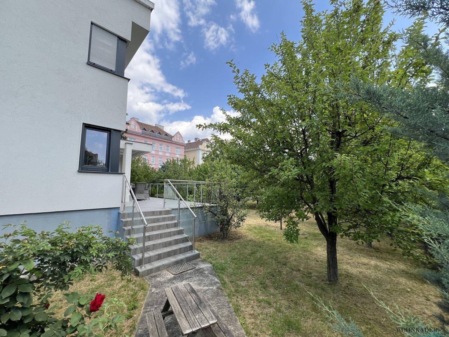 Grüner Gartenbereich mit Bäumen und Steintreppe, die zum Haus hinaufführt.