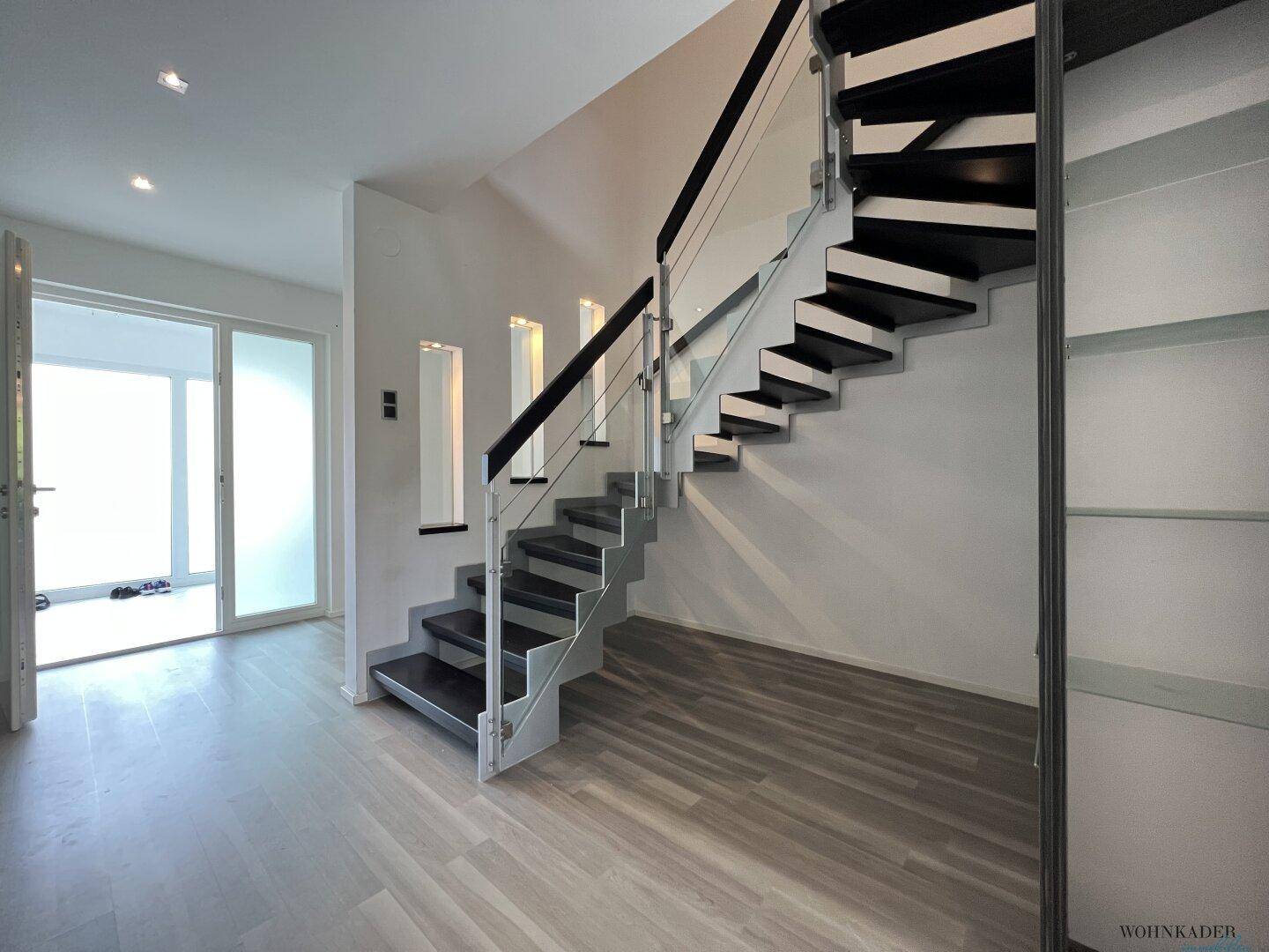 Moderner Eingangsbereich mit eleganter Treppe und Glasgeländer, hell und offen gestaltet.