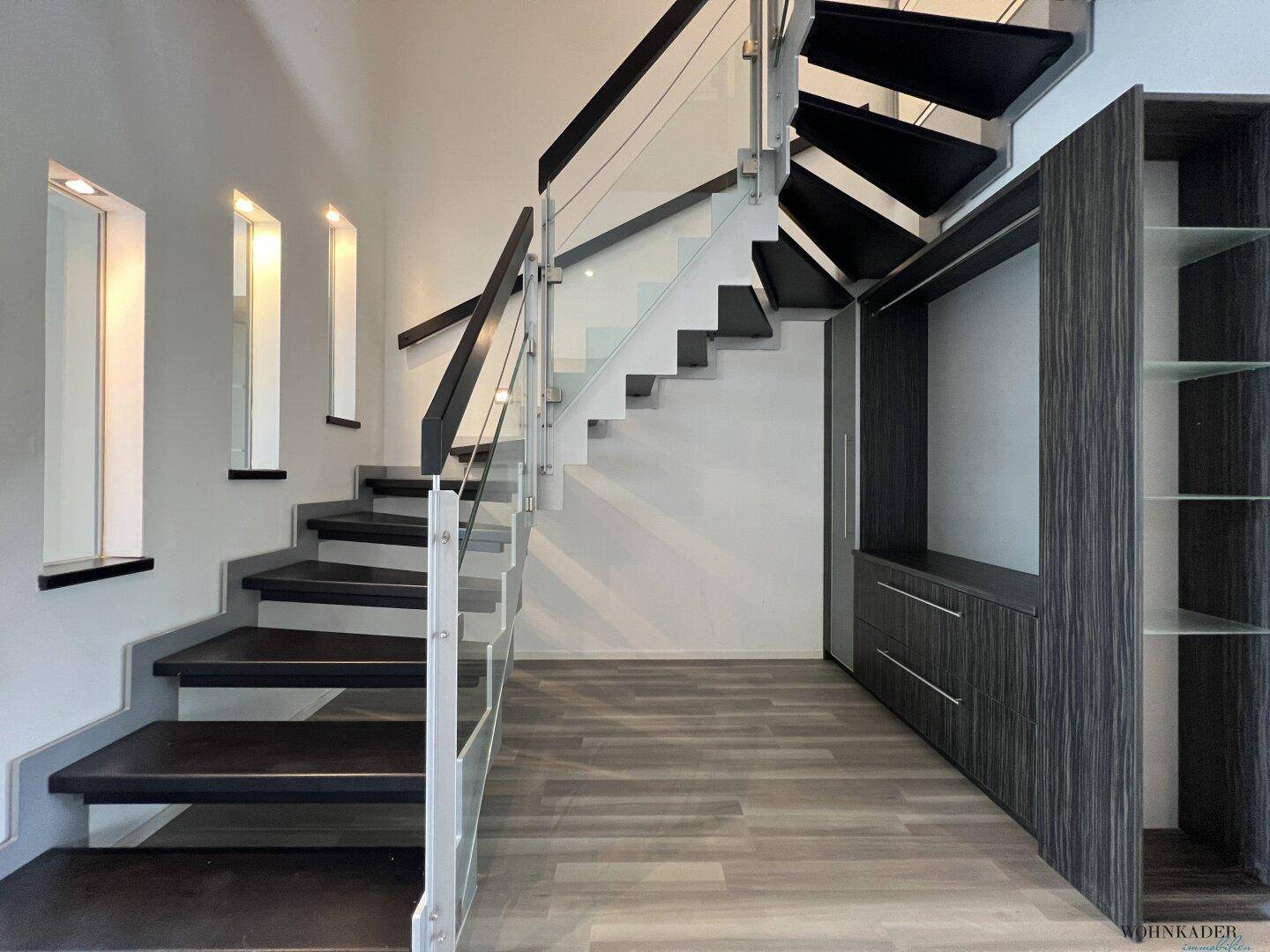 Heller Flur mit moderner Treppe, Glasgeländer und integriertem Stauraum.
