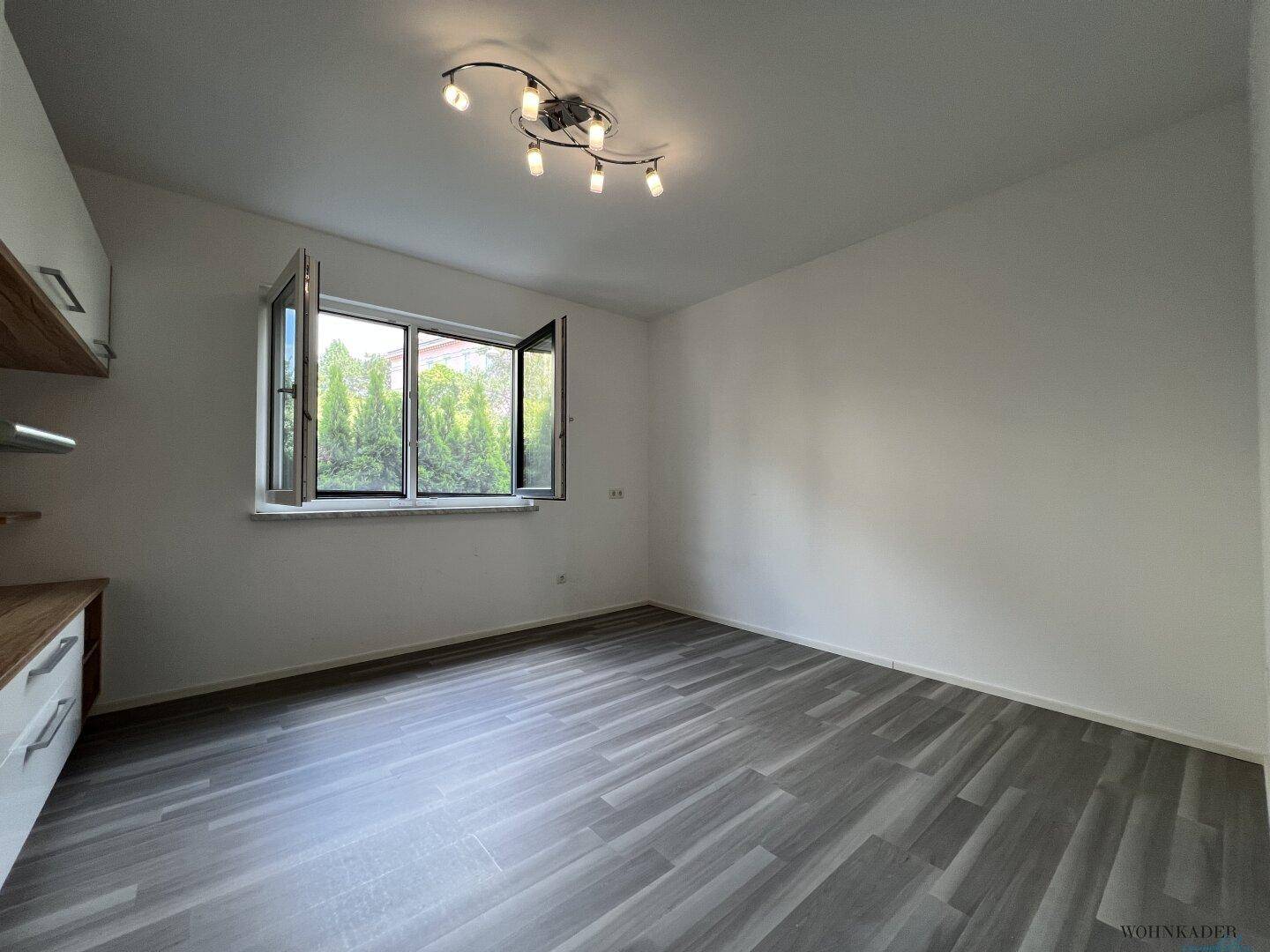 Heller Raum mit Fensterblick ins Grüne und praktischen Einbauschränken, ausgestattet mit modernem Laminatboden.