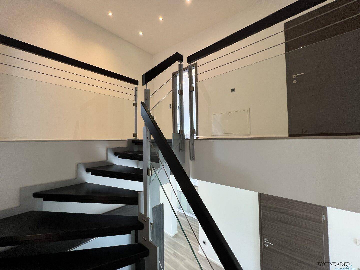 Moderne Treppe mit dunklen Stufen und Glasgeländer, die zu den oberen Räumen führt.