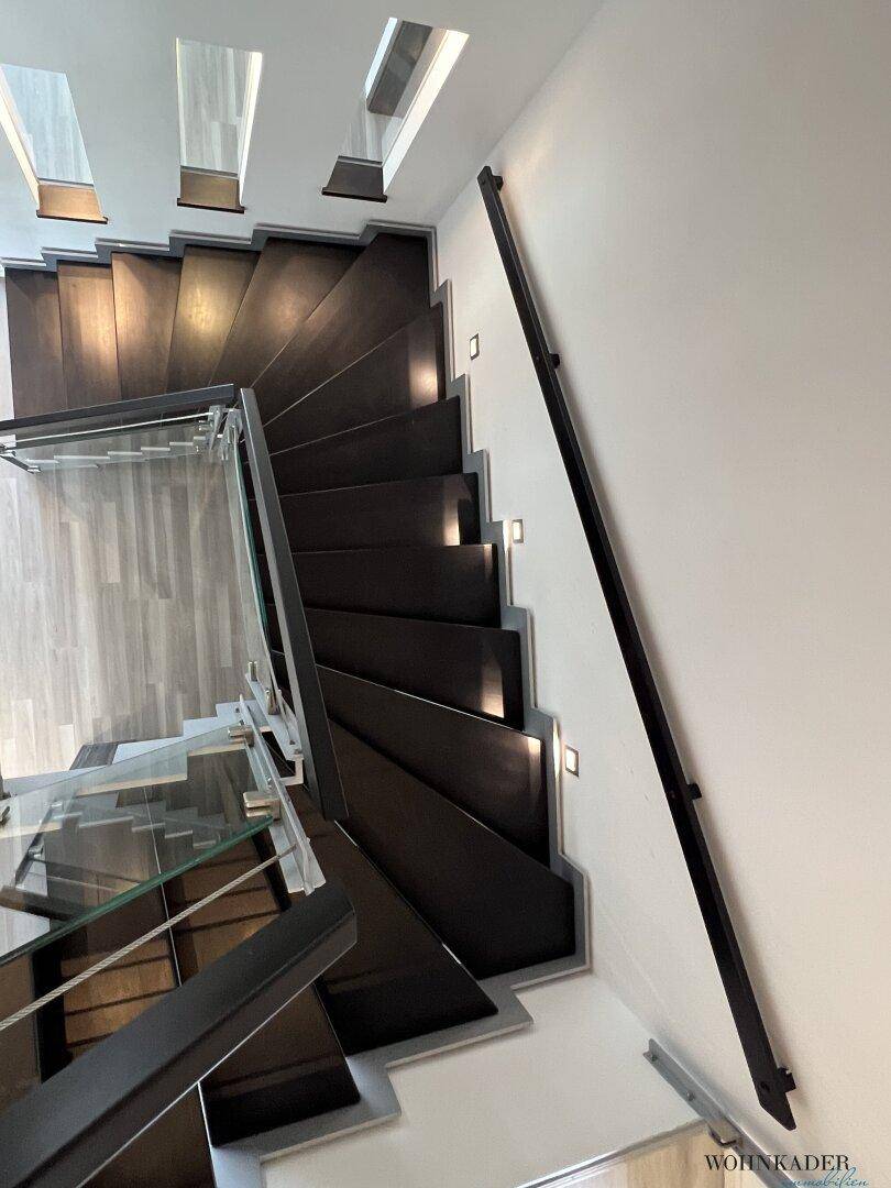 Elegante Wendeltreppe mit dunklen Holzstufen und integrierter Beleuchtung, umgeben von Glasgeländer.