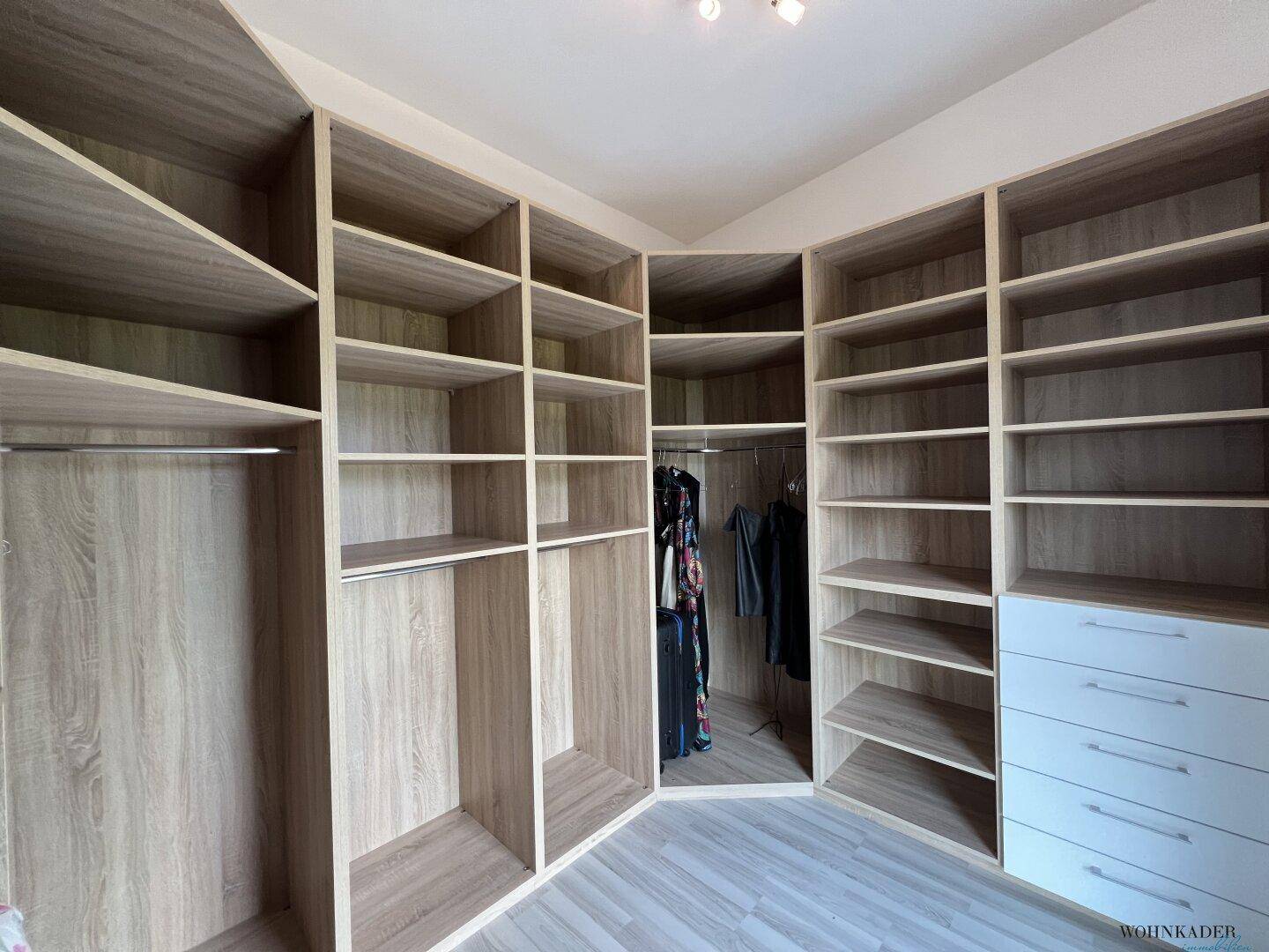 Großzügiger begehbarer Kleiderschrank mit maßgefertigten Regalen und Schubladen in heller Holzoptik.