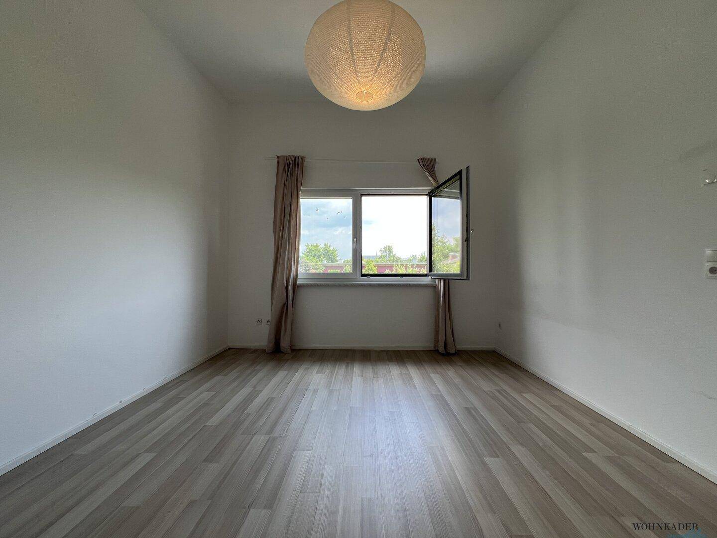 Heller Raum mit großem Fenster, hellem Laminatboden und einer modernen Deckenleuchte, ideal für individuelle Gestaltung.