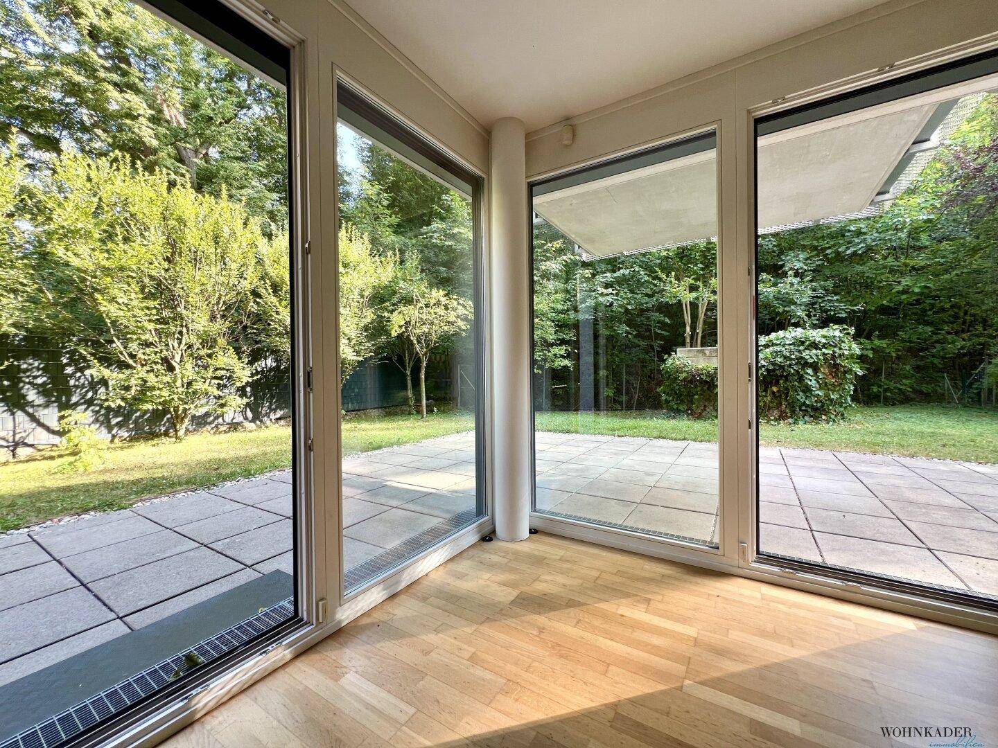 Heller Raum mit Parkettboden und großen Fensterfronten, die den Blick in den Garten freigeben.
