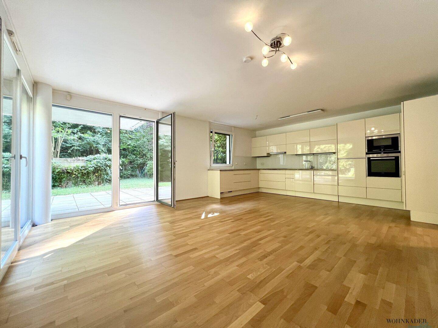 Offener Wohnbereich mit moderner Einbauküche, Parkettboden und Zugang zur Terrasse.