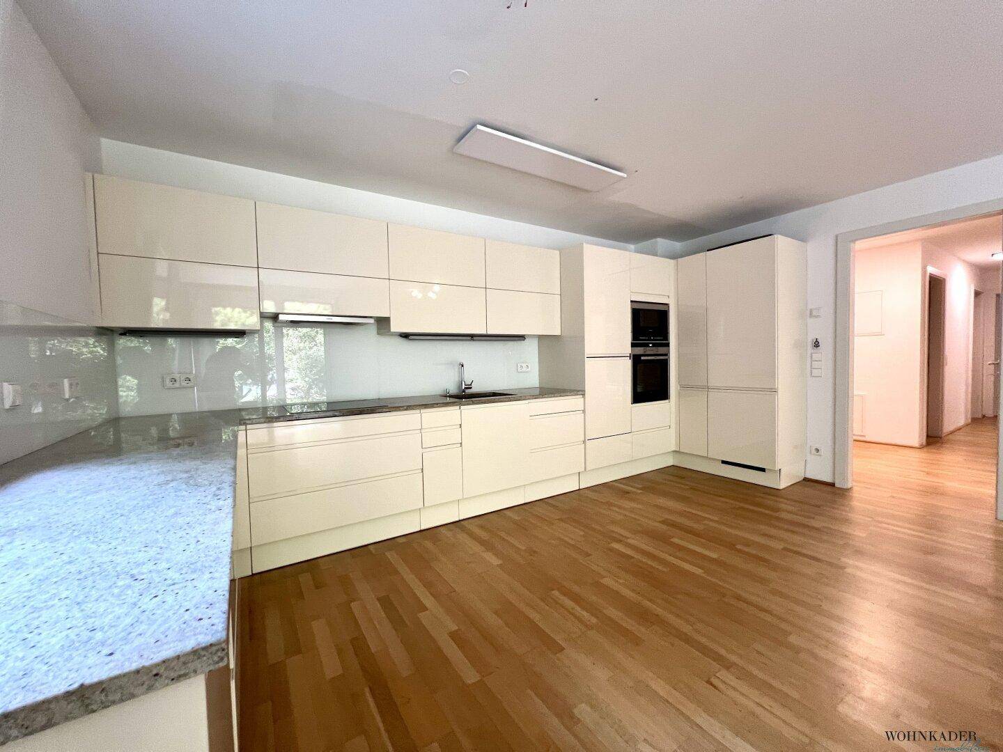 Moderne Einbauküche mit hellen Hochglanzfronten, Granitarbeitsplatte und Parkettboden.
