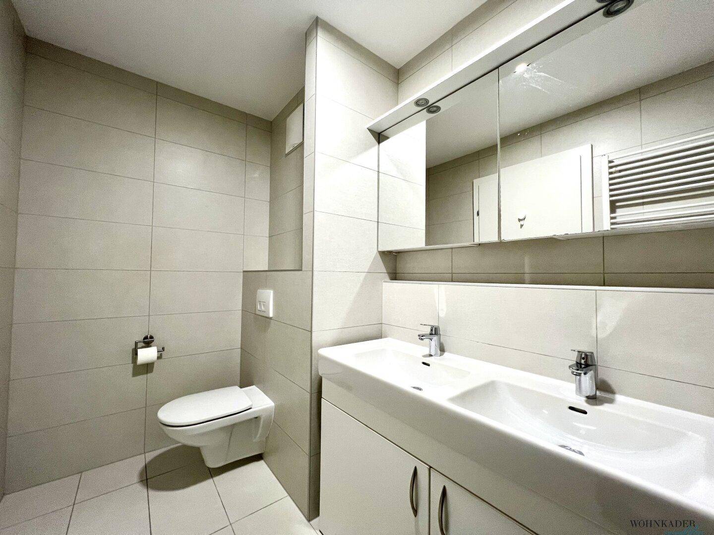 Modernes Badezimmer mit Doppelwaschbecken, Badewanne, WC und hellen Fliesen.