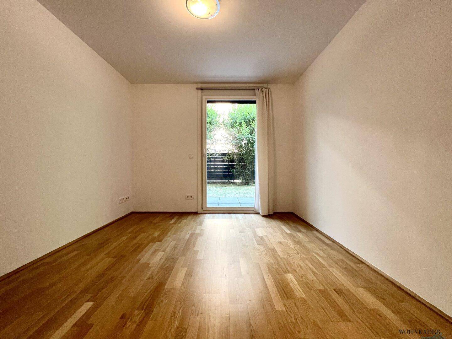 Geräumiges Schlafzimmer mit Parkettboden und großem Fenster mit Blick ins Grüne.