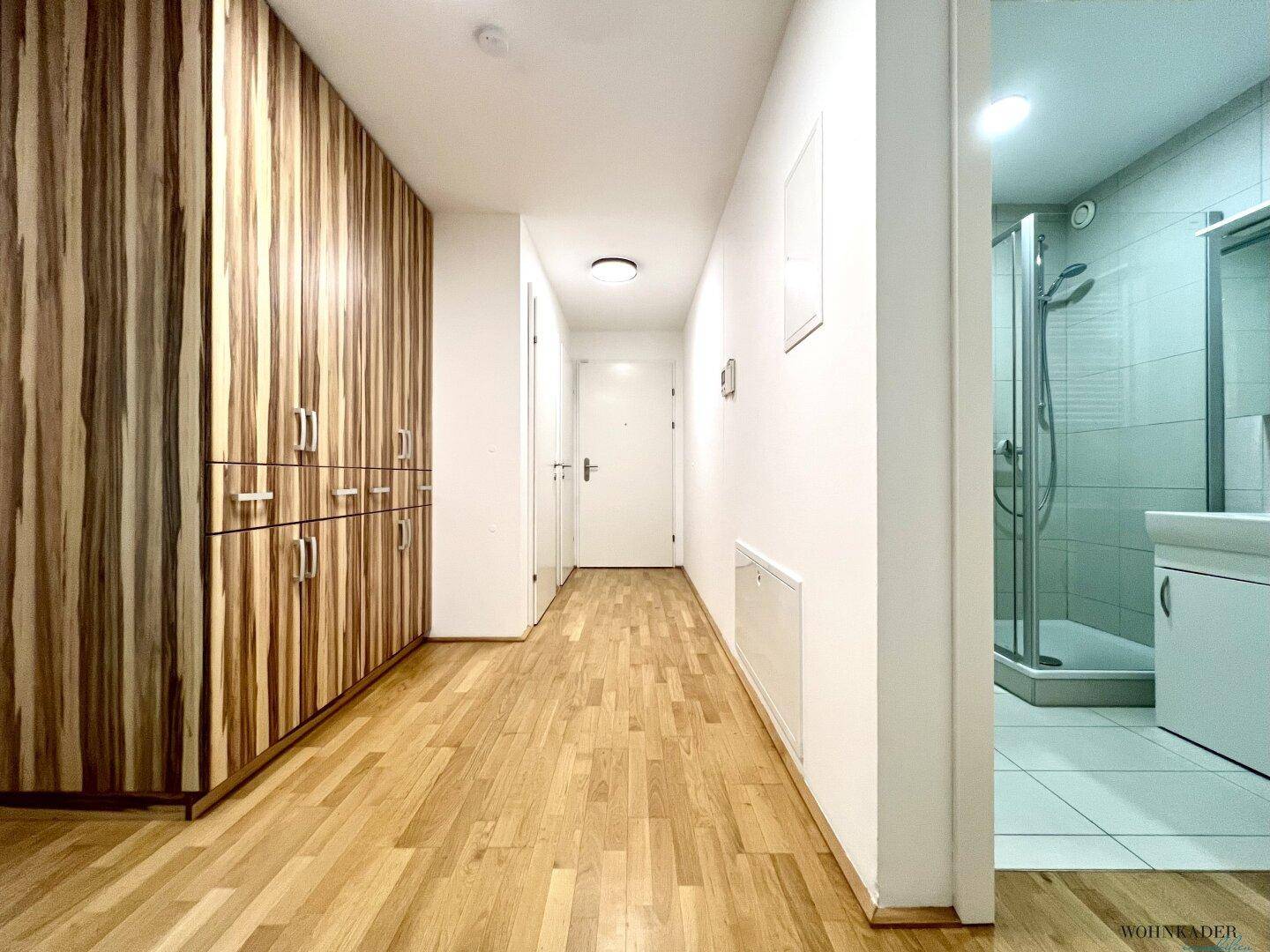 Langer Flur mit Parkettboden, Einbauschrank und Zugang zu einem Badezimmer mit Dusche.