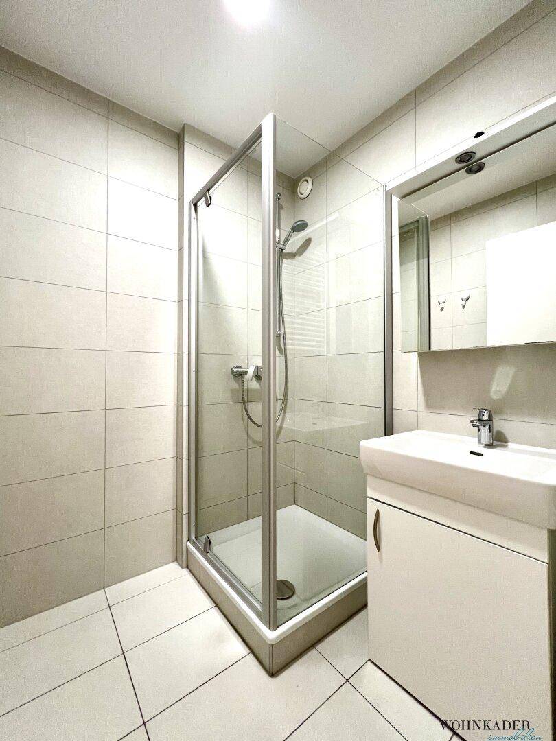 Modernes Badezimmer mit Duschkabine, Waschbecken und hellen Wand- und Bodenfliesen.