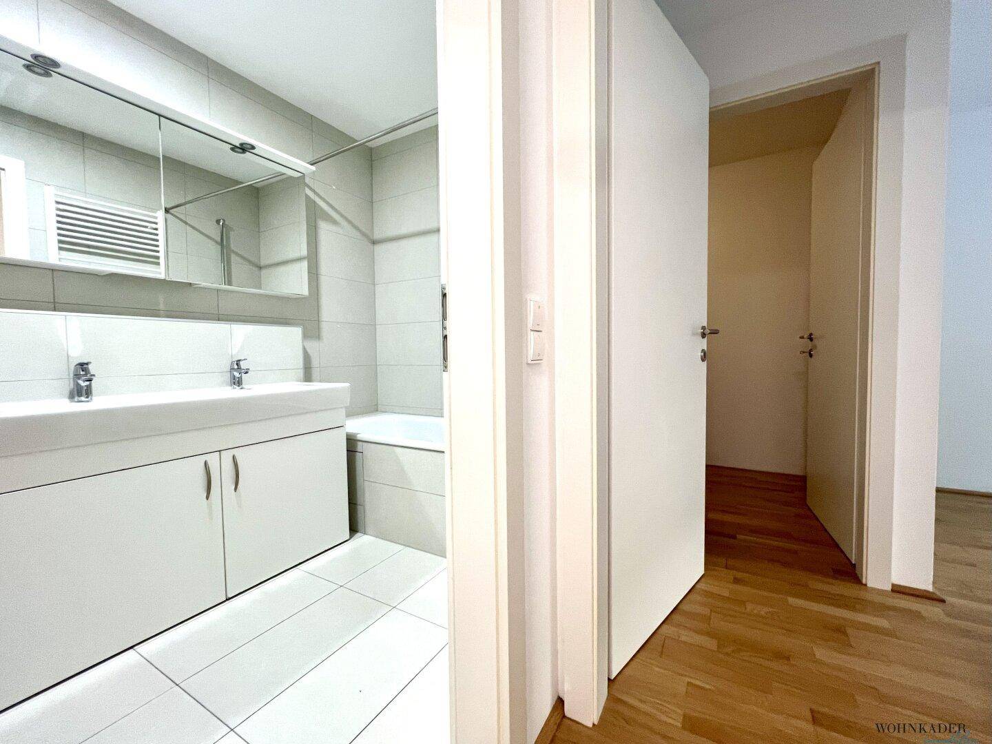 Badezimmer mit Doppelwaschbecken und Badewanne, sichtbar durch die offene Tür.