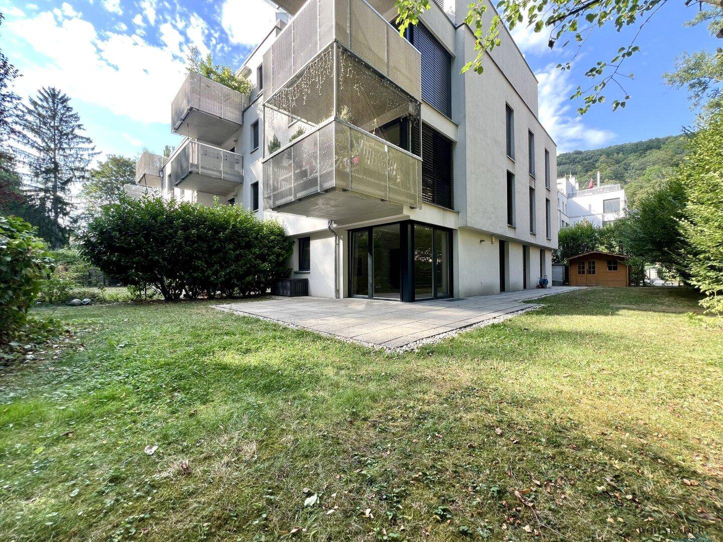 Weitläufiger Gartenbereich mit Rasenfläche und einer gepflasterten Terrasse vor dem modernen Gebäude.